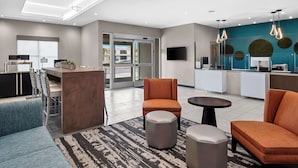 Un moderno vestíbulo de hotel con recepción, zona de estar y kitchenette.