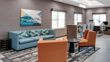 A modern lobby with a sofa, armchairs, a coffee table, and a dining area.