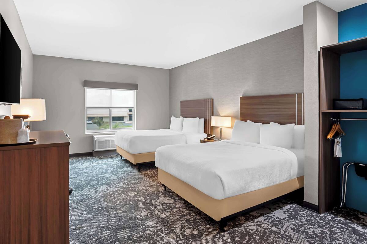 A hotel room with two beds, a desk, a window, and a wardrobe.