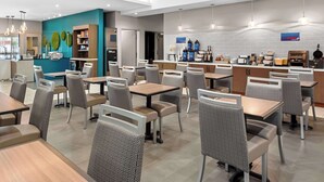 Un restaurante moderno de hotel con varias mesas y sillas, una zona de cocina y un mostrador de recepción.