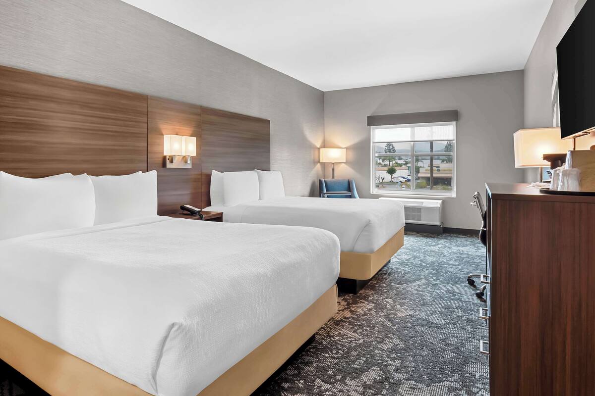 A hotel room with two beds, a desk, a chair, and a TV.
