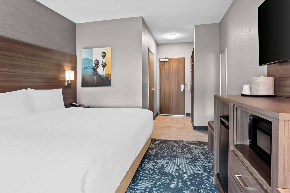 A hotel room with a large bed, a TV, a painting, and a wooden cabinet.