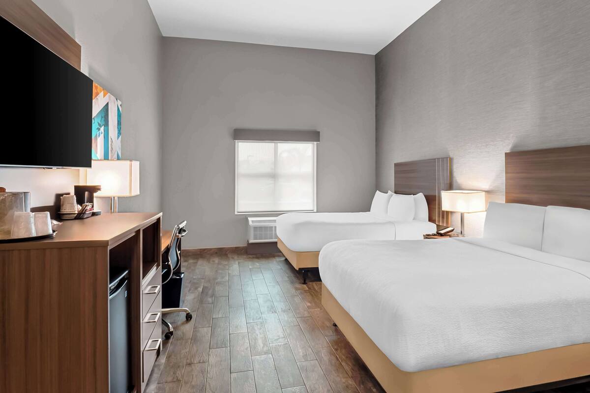 A hotel room with a large bed, a desk with a flat-screen TV, a window, and a wall-mounted artwork.