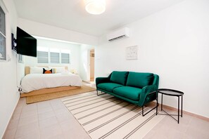A modern bedroom with a bed, a green sofa, a small table, and a TV mounted on the wall.