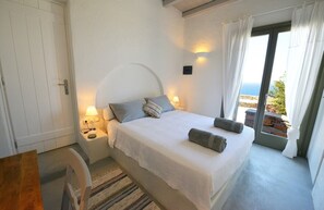 Une chambre à coucher avec un lit, des lampes de chevet, une table de nuit, une fenêtre avec des rideaux et une vue sur l’extérieur.