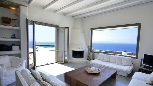 A spacious living area with a fireplace, white furniture, and large windows offering a view of the sea. - 5 Bedroom Spectacular sunset view villa (Coressia)