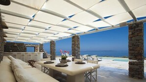 An outdoor patio with a dining area, stone pillars, and a view of the sea. - 5 Bedroom Spectacular sunset view villa (Coressia)