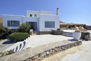 Un bâtiment moderne aux murs blancs, doté d’une façade en pierre, d’une cheminée et d’un espace piscine avec des chaises longues.