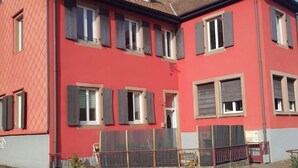 A red two-story building with multiple windows and a tiled roof. - Petit Appartement Lumineux et Indépendant (Lalaye)