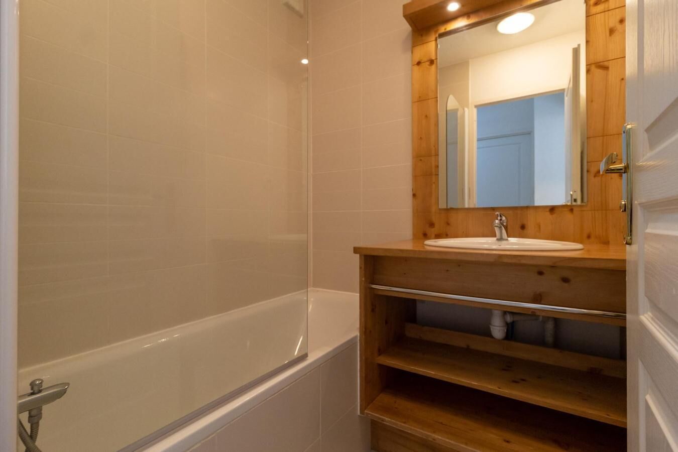 Een badkamer met een bad, een houten wastafelmeubel en een spiegel.