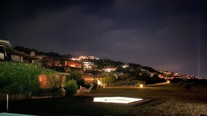 Een nachtzicht van een woongebied met een zwembad, een terras met tuinmeubels, en huizen met verlichte ramen.