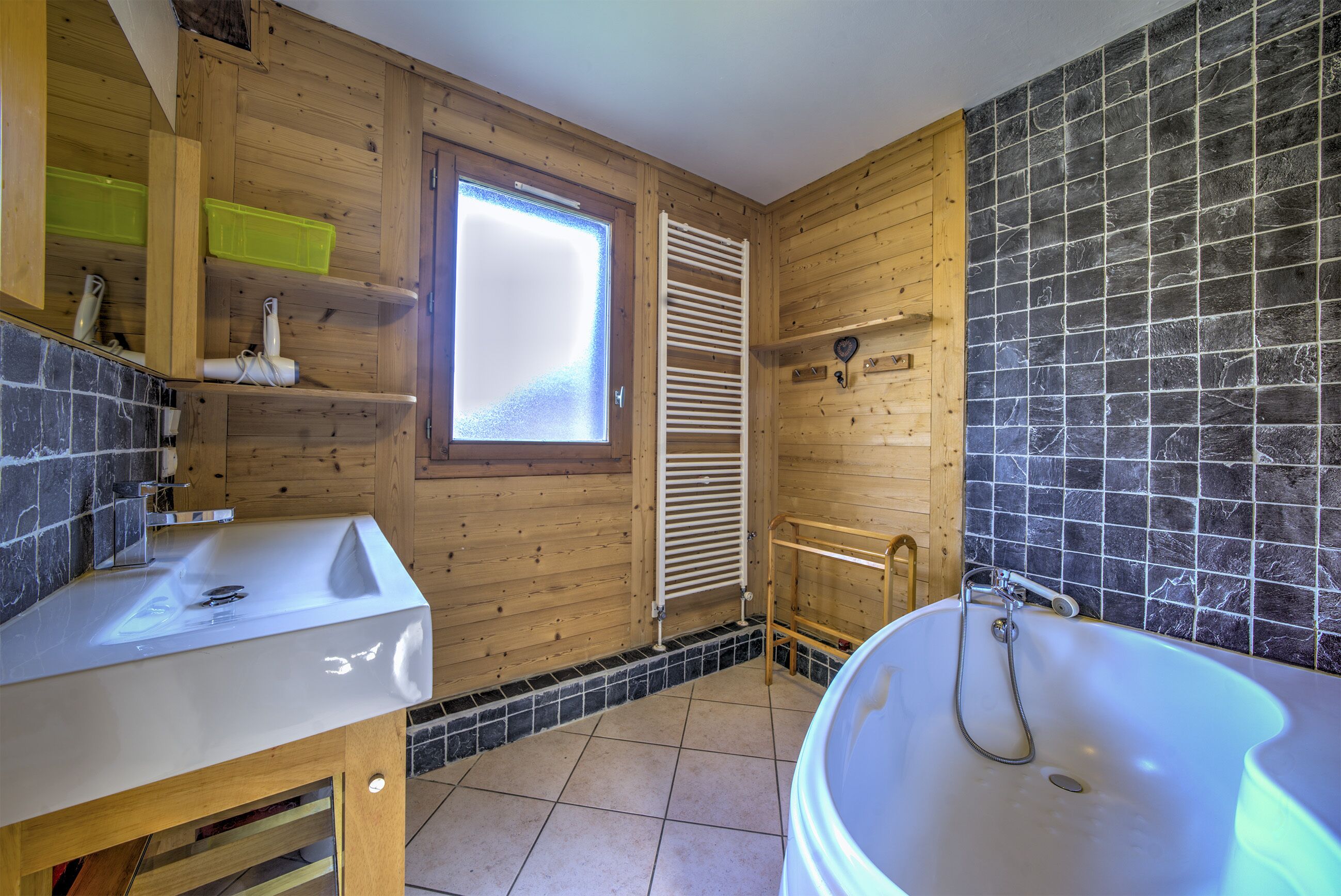 Une salle de bain rustique, avec des murs en bois, un lavabo blanc, une baignoire et une fenêtre.