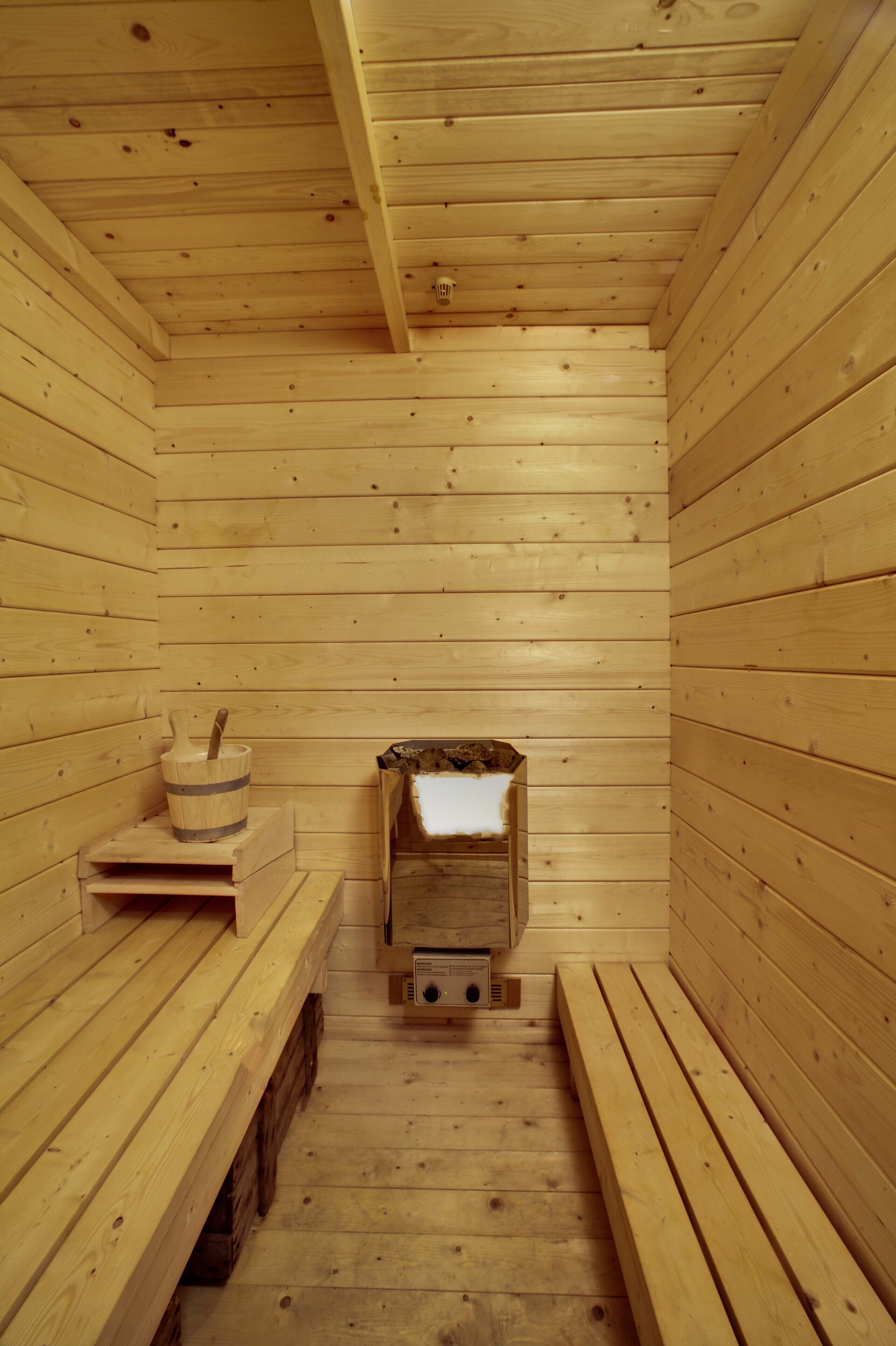 Eine Sauna mit Holzwänden und -bänken, ein Holzbecken mit Bürste und ein Ofen.