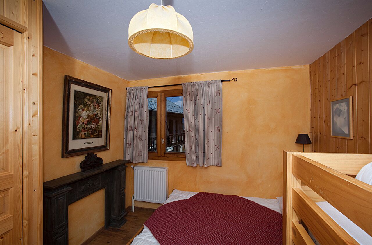 A bedroom with a wooden bed, a radiator, a window with curtains, and a painting on the wall.