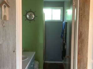 A narrow hallway with a green wall, a wooden door frame, a small window, and a door leading to a bathroom.