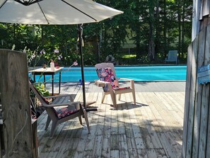 A wooden deck with a pool, lounge chairs, and a table with a flower vase.