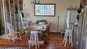 A rustic dining area with a wooden table, chairs, and a window overlooking a forest. - Swimmin pool movie stars &a c’ment pond- jc ma gee (Shédiac)