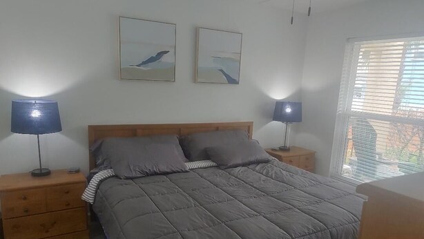 Une chambre à coucher comprenant un lit, deux tables de chevet, deux lampes fixées au mur et deux tableaux encadrés.