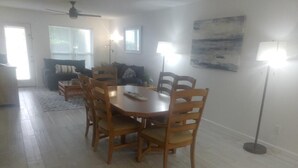Un coin repas avec une table ronde en bois et des chaises, un ventilateur de plafond et un tableau accroché au mur.