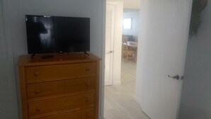 Une pièce avec une commode en bois, un téléviseur à écran plat posé dessus, et une porte blanche donnant sur une autre pièce.