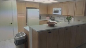 Une cuisine avec des meubles de rangement en bois, un plan de travail blanc, un four à micro-ondes, une cuisinière et une poubelle.