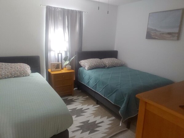 A bedroom with two beds, a nightstand, a lamp, a painting, and a patterned rug. - GROUND FLOOR UNIT 110 (South Padre Island)