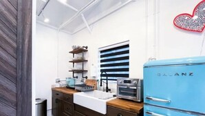 Eine kleine Küche mit einem blauen Galanz-Kühlschrank, einer weißen Spüle, Holzschränken und einem gestreiften Fenster.