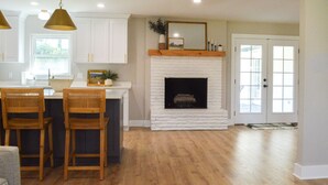 A kitchen with white cabinets, a wooden island with two chairs, a fireplace, and a door leading to a balcony. - Spacious, Remodeled Home in the Heart of Hammond (Hammond)