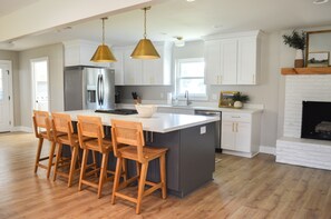 A spacious kitchen with a large island, wooden bar stools, stainless steel appliances, and pendant lighting. - Spacious, Remodeled Home in the Heart of Hammond (Hammond)