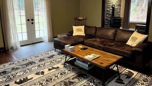 A living room with a brown leather sofa, a wooden coffee table, patterned rugs, and a stone fireplace. - Cozy Home With Fire Place 10 Mins From Hunter Mountain (Palenville)