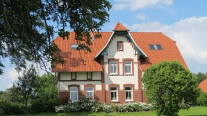 Une maison à deux étages, avec un toit recouvert de tuiles rouges, des murs blancs et de nombreuses fenêtres.