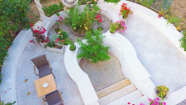 A circular outdoor seating area with a table and chairs, surrounded by flower planters and a small fountain.