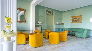 A room with yellow armchairs, a green sofa, a marble floor, and a mirror with an ornate frame.