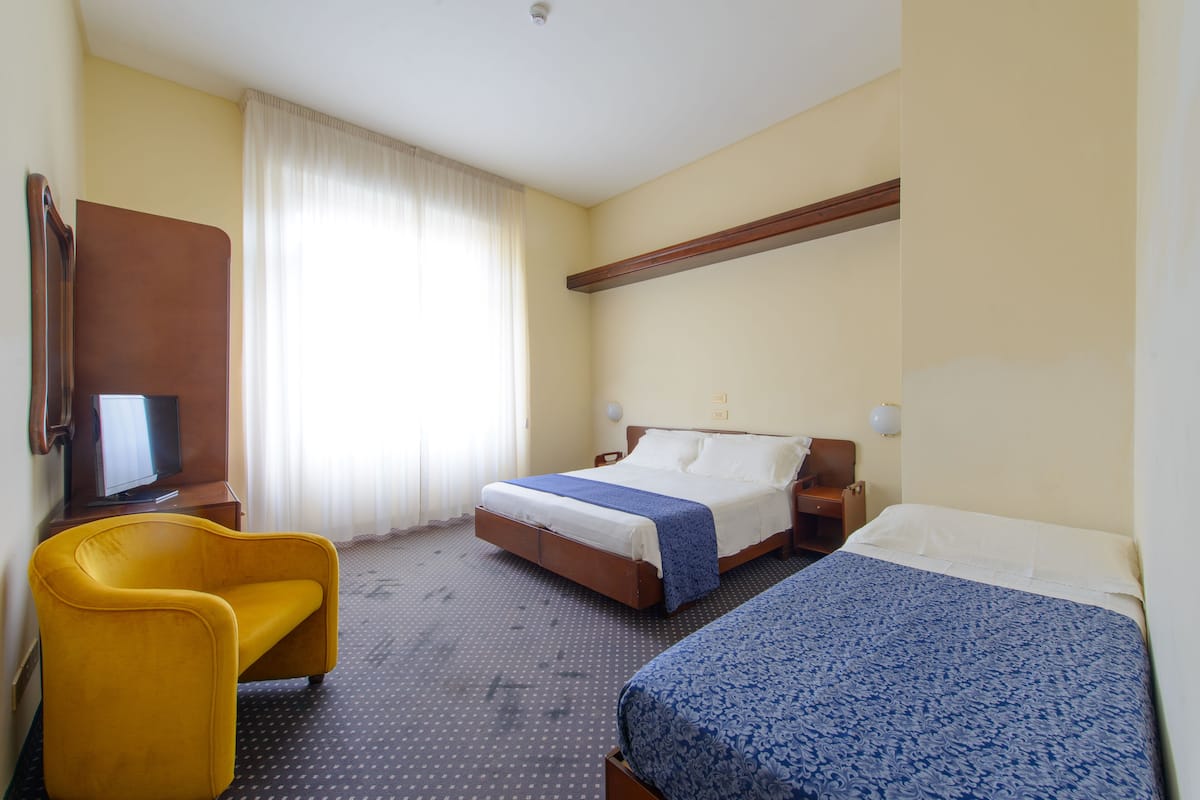 Quarto de hotel com duas camas, uma cadeira, uma televisão e uma janela com cortinas.