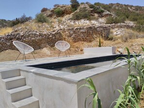 A modern outdoor pool area with two white chairs, a stone wall, and a staircase leading to a higher level. - Cycladic-style house, pool, 10 minutes to the beach (Galissas)