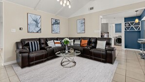 A modern living room with a sectional sofa, a glass coffee table, and abstract wall art.