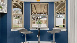 A corner room with two bar stools, a round table, and a window with a view of the backyard.