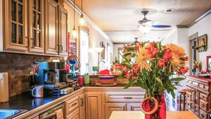 A kitchen with wooden cabinets, a coffee maker, and a vase with flowers on the table. - Two Couples, 2 Primary Suites, 1 BoHo GardenHouse (Pensacola)