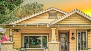 A single-story house with a gabled roof, a front porch, and a small window with a metal grill. - Two Couples, 2 Primary Suites, 1 BoHo GardenHouse (Pensacola)