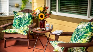 A porch with two wooden chairs, a small table with a vase of flowers, a mug, and a plate with cookies. - Two Couples, 2 Primary Suites, 1 BoHo GardenHouse (Pensacola)