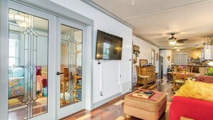 A spacious living room with a large television, wooden flooring, and a red sofa. - Two Couples, 2 Primary Suites, 1 BoHo GardenHouse (Pensacola)