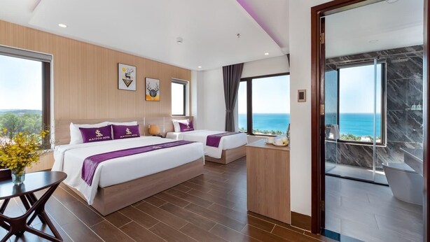 Una habitación de hotel moderna con una cama grande, una cama más pequeña, un escritorio y vistas al océano.