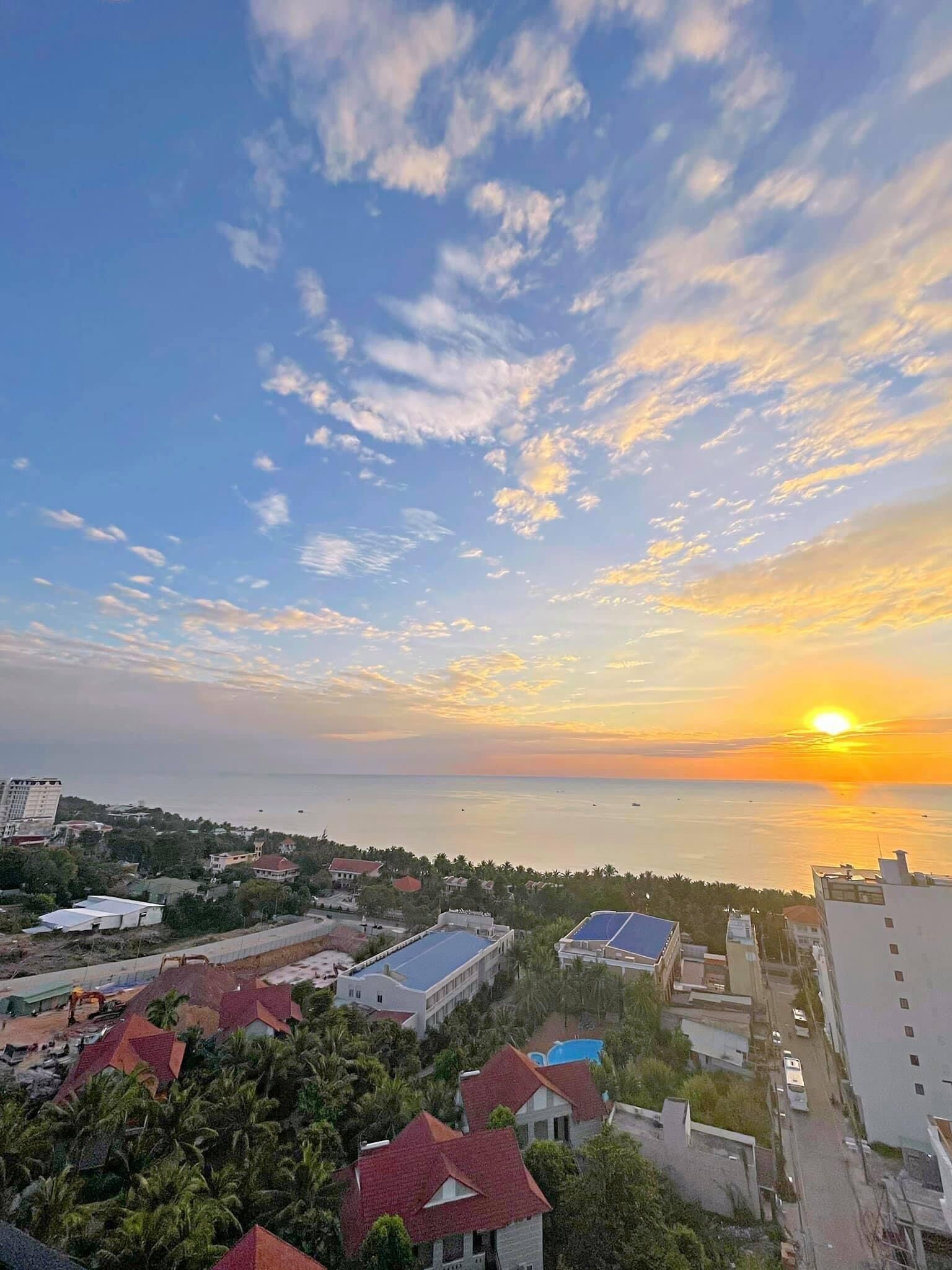 A coastal cityscape with buildings, a clear sky, and a sunset over the sea.