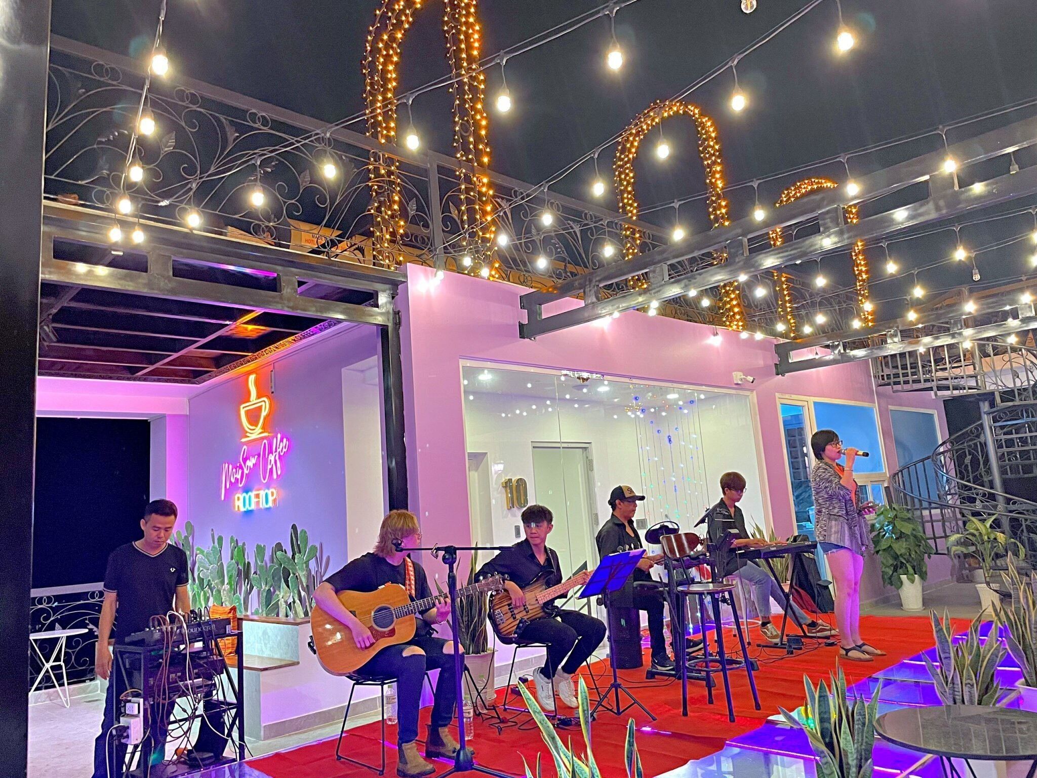 A stage with musicians performing, surrounded by plants and a staircase.