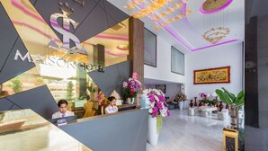 Un moderno vestíbulo de hotel con mostrador de recepción, un espejo grande y diversas plantas decorativas.