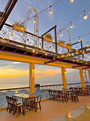 An outdoor dining area with tables and chairs, decorative lights, and a view of the sea. - MAISON HOTEL PHU QUOC (Phu Quoc)