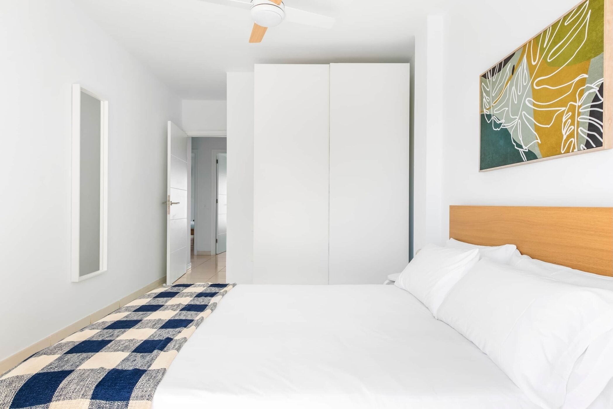 Een slaapkamer met een bed, een plafondventilator, een kledingkast en een schilderij aan de muur.