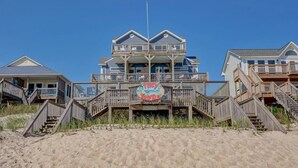 A beachfront property with a multi-level wooden structure, a sign reading "TIPSY TURTLE," and a sandy beach in the foreground. - Tipsy Turtle North- Oceanfront Oasis - Pool - Dog Friendly (Surf City)