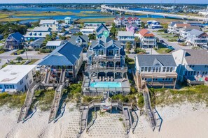 A coastal residential area with multiple houses, a large central building with a swimming pool, and a beach in the foreground. - Tipsy Turtle North- Oceanfront Oasis - Pool - Dog Friendly (Surf City)