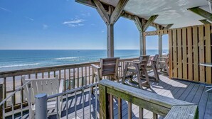 A wooden deck with a view of the ocean, featuring a covered seating area with chairs and a table. - Tipsy Turtle North- Oceanfront Oasis - Pool - Dog Friendly (Surf City)